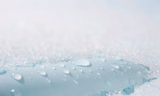 Extreme macro of clear water droplets beading on a cool pale blue ceramic surface with crystalline salt edges
