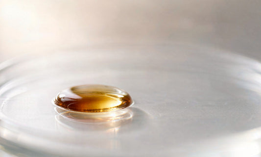 Extreme macro of a single amber oil droplet on clean laboratory glass with shallow depth of field