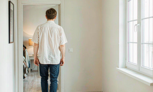 Man seen from behind walking down a softly lit home hallway toward a warm lamp in the evening