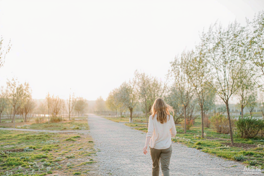 Woman with blonde hair walking a gravel park trail at sunrise, seen from behind