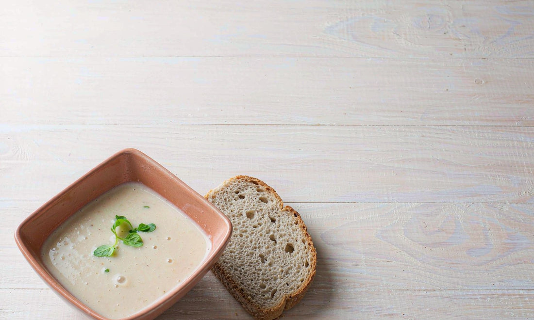Top-down view of a simple bowl of warm soup with herbs on a pale wooden table, representing comfortable digestion