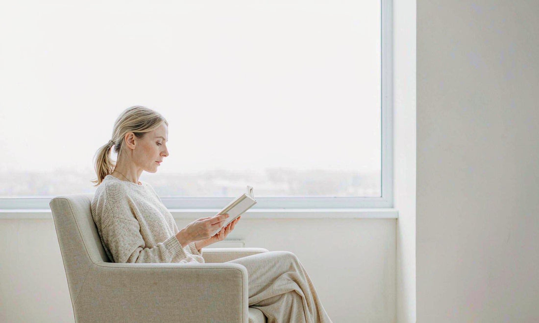 A person reading in an armchair by a large bright window, representing calm and relaxation