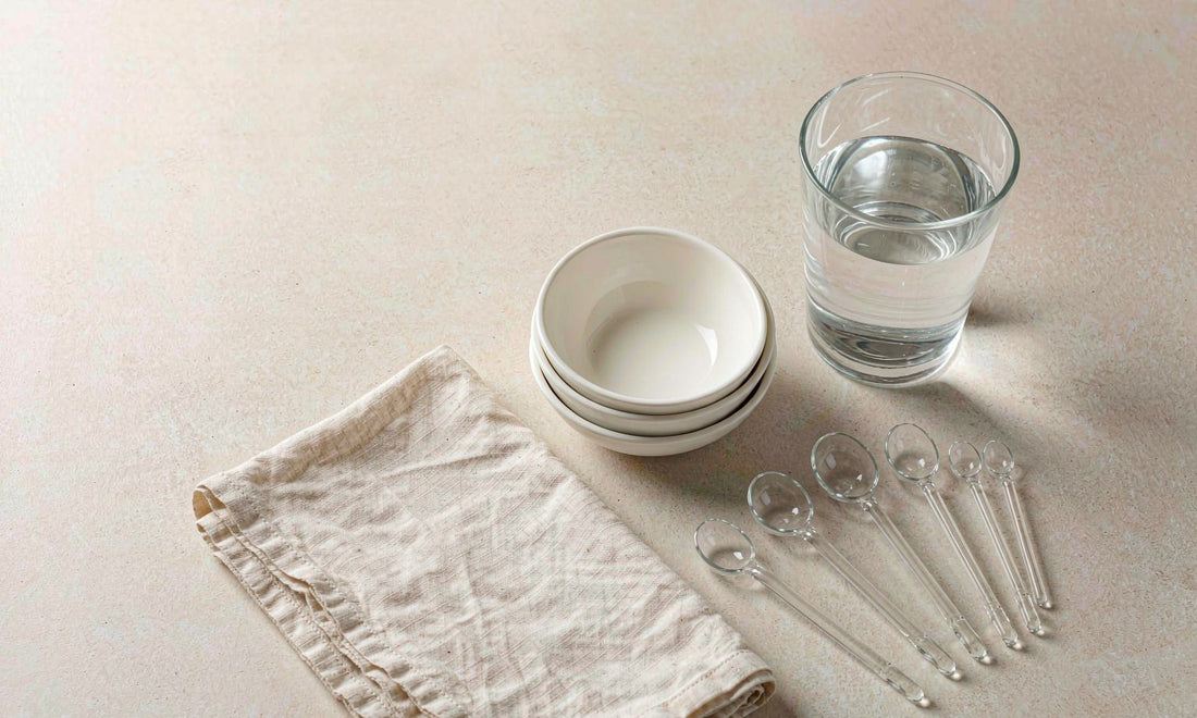 Measuring spoons, ceramic bowls and a glass of water laid out neatly on a beige counter to show careful portioning