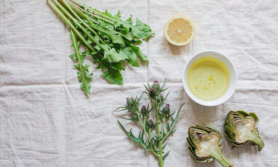 Flat lay of dandelion greens, milk thistle, lemon, olive oil and artichokes on linen