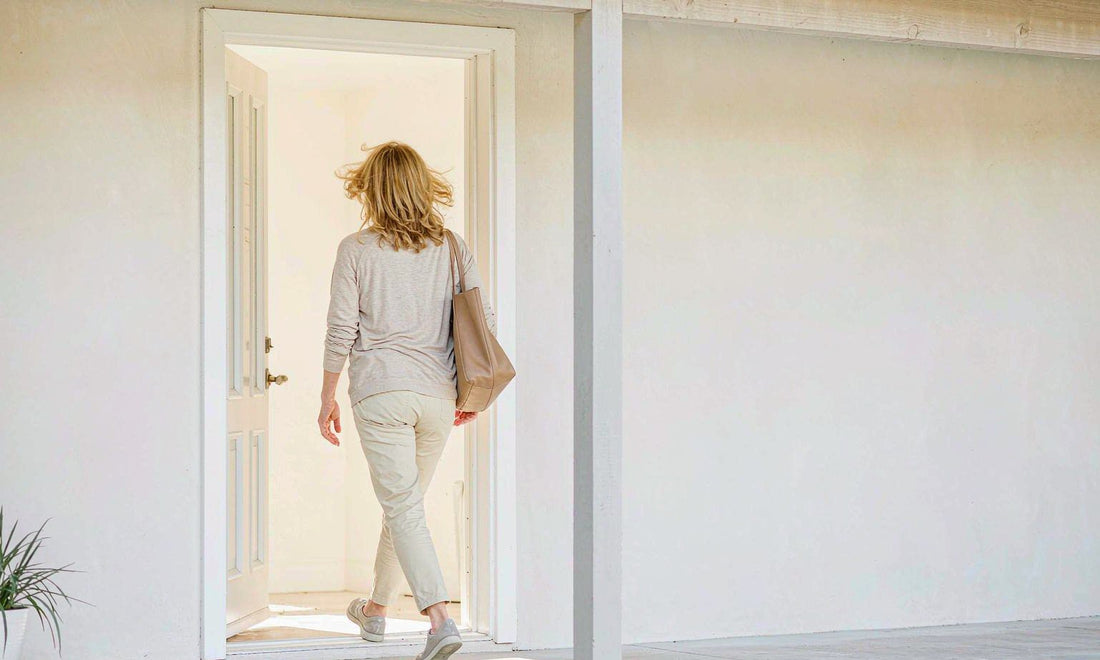 Mature woman seen from behind stepping outside in sneakers with a tote bag in soft morning light