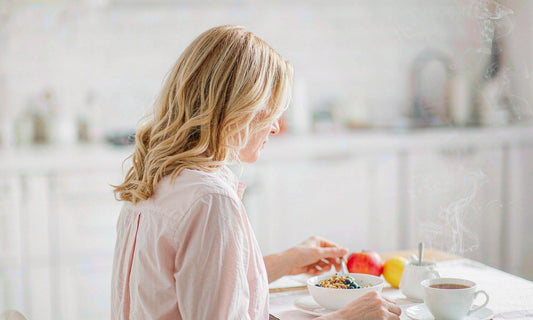 Woman with light blonde hair seated at a bright breakfast table with yogurt, fruit and tea