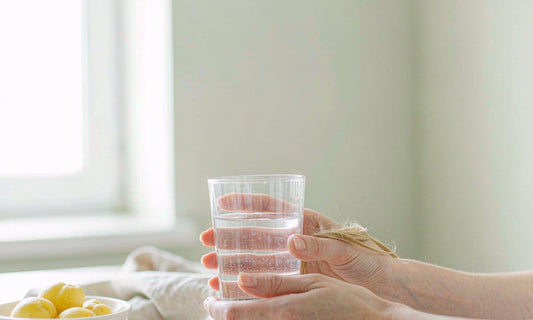 Hands with fair light skin holding a glass of water in soft morning kitchen light
