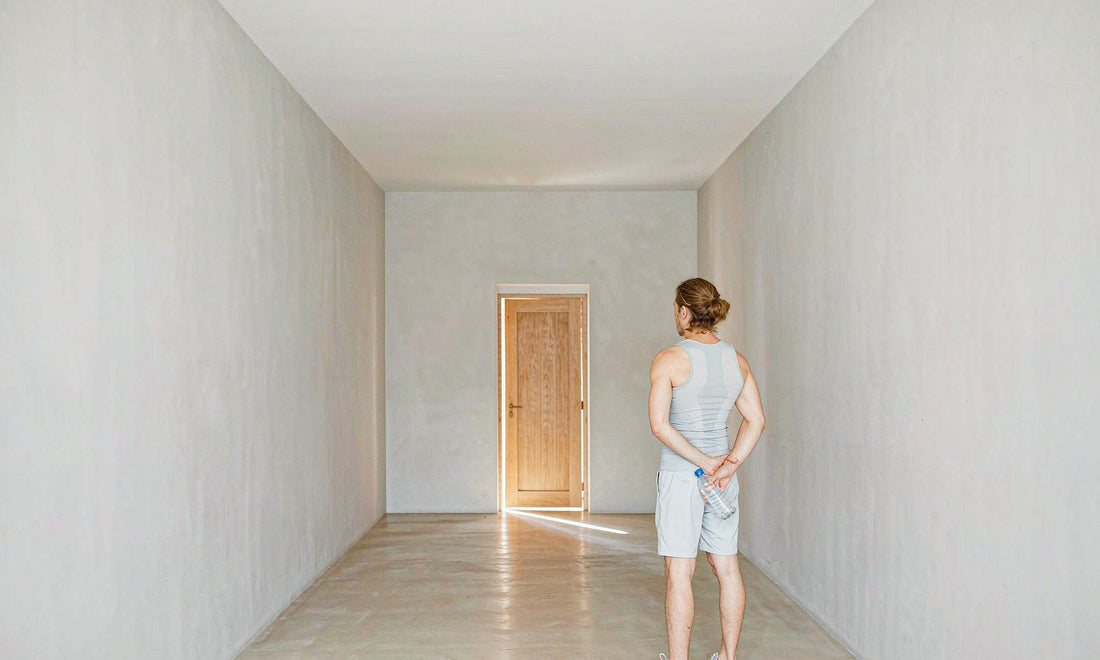 An athlete seen from behind in a bright hallway facing the front door with a water bottle at sunrise
