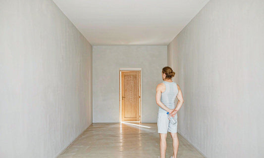 An athlete seen from behind in a bright hallway facing the front door with a water bottle at sunrise