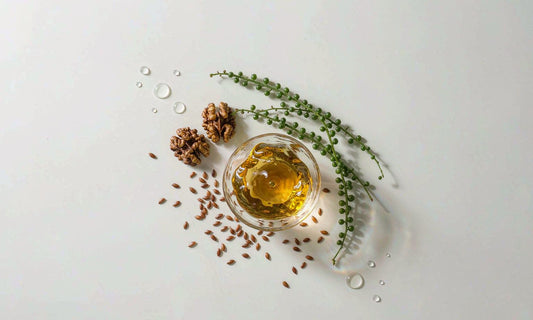 Top view of golden omega oil glass dish with walnuts, flaxseed and green sea stems on pale surface