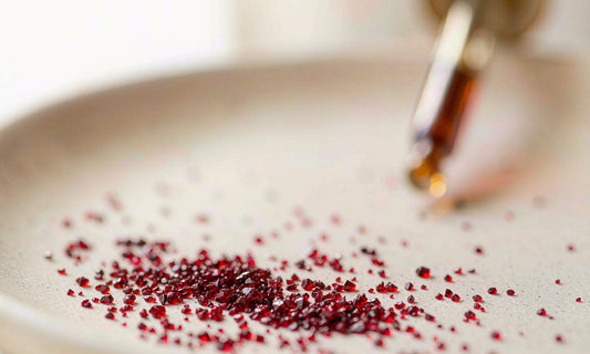 Macro view of fine crimson supplement crystals scattered on a matte ceramic plate with a blurred dropper