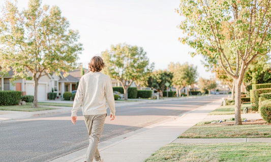 Person seen from behind taking a relaxed walk on a sunny suburban sidewalk after a midday meal