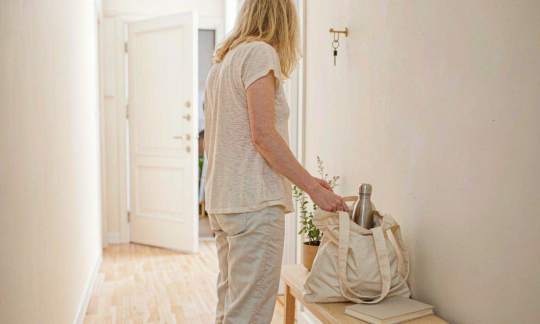 Woman seen from behind at a bright entryway setting down a tote bag with a water bottle