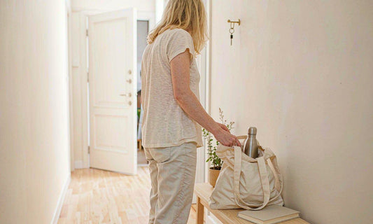 Woman seen from behind at a bright entryway setting down a tote bag with a water bottle