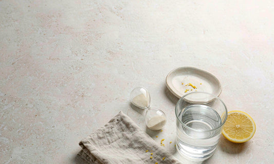 Hourglass beside a glass of water and lemon slice on a pale stone countertop in morning light