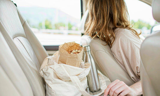 Person seen from behind in a car seat beside a tote bag of nuts and a steel bottle