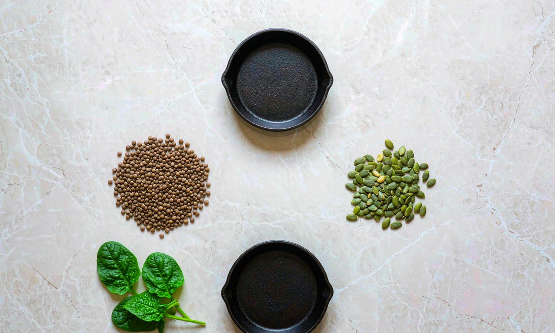 Overhead flat lay of lentils, spinach, pumpkin seeds and cast iron skillets on pale marble for iron-rich eating