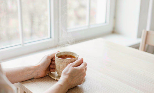 Hands holding a warm mug of herbal tea by a bright window, a caffeine free afternoon wind down.