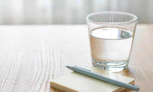 A blank notepad, slim pen and glass of water on a pale oak table in soft daylight
