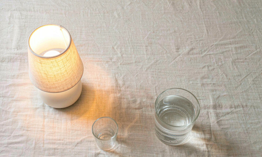 A glass of water beside a dim warm lamp on a nightstand in a quiet bedroom at night