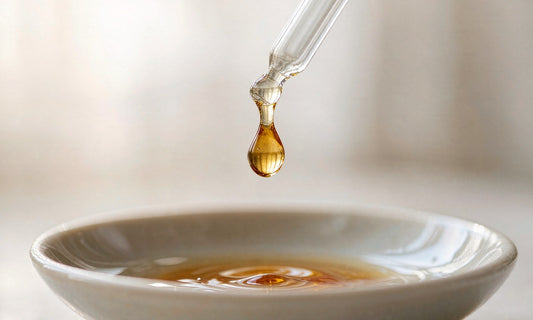 Macro close-up of an amber liquid drop falling from a glass dropper into a small ceramic dish
