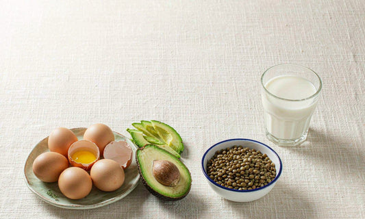 An overhead flat lay of eggs, avocado, lentils and a glass of milk on ivory linen