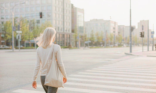 Woman with a canvas tote bag seen from behind crossing a bright urban crosswalk in morning light