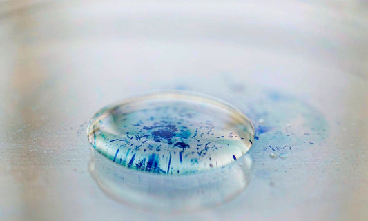 Macro view of deep blue pigment crystals dissolving in a clear water droplet on glass