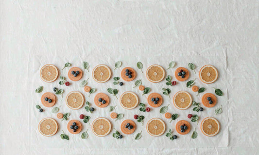 Semi-abstract overhead grid of citrus slices, berries and leafy greens on a soft white surface