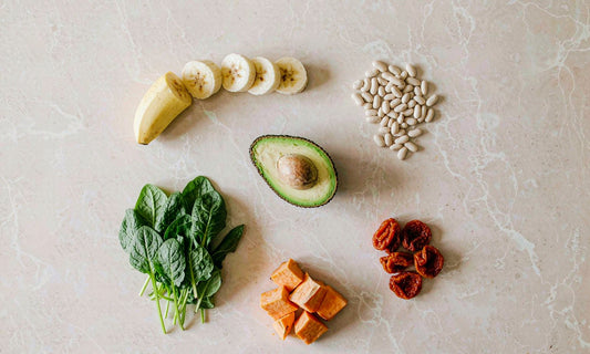 Potassium-rich foods on pale stone: banana, avocado, white beans, spinach, sweet potato and apricots