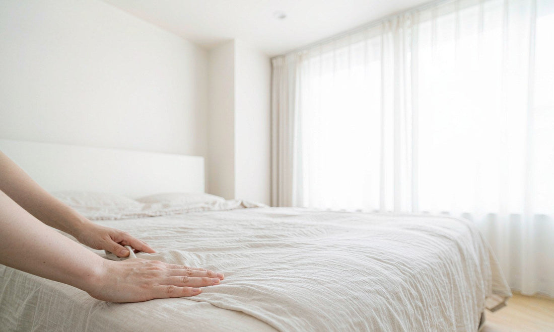 Hands smoothing linen bedding in a bright minimal bedroom, representing a restful sleep routine