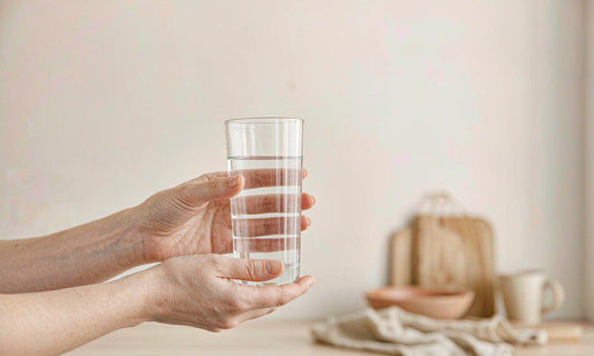 Fair-skinned hands holding a clear glass of water in a bright minimal kitchen
