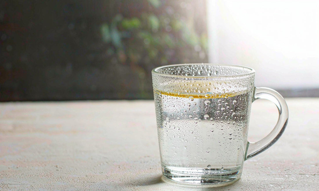Macro of condensation droplets on a clear glass of water on a pale stone windowsill in soft morning light