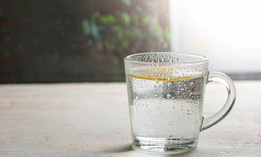 Macro of condensation droplets on a clear glass of water on a pale stone windowsill in soft morning light