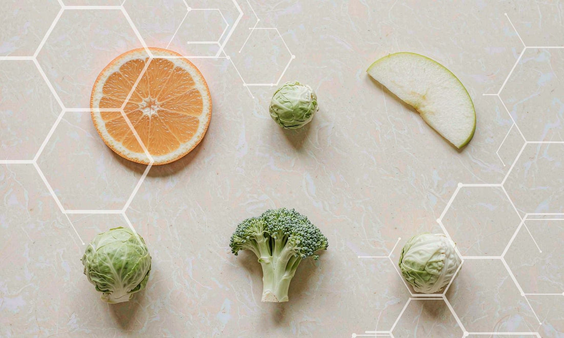 Overhead flat lay of orange and apple slices with broccoli and Brussels sprouts on pale stone