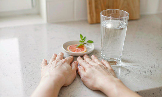 Relaxed hands resting on a light quartz kitchen counter beside a glass of water and a small dish of citrus