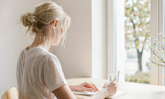 Woman seen from behind planning her new year reset at a sunlit desk with a glass of water