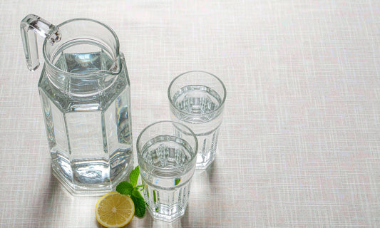 Overhead flat lay of a glass pitcher and two glasses of water with lemon and mint, simple daily hydration.