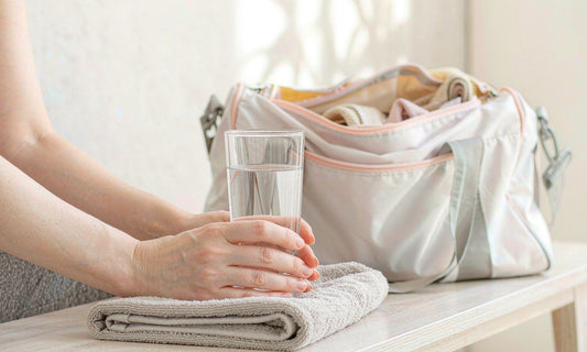 Relaxed hands holding a glass of water beside a towel and gym bag after training