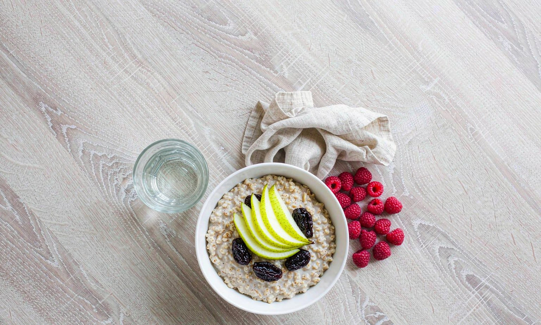 Overhead flat lay of oatmeal with pear slices, prunes and a glass of water, the fiber and fluid base of a kids routine