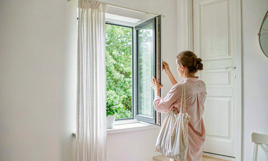 Person seen from behind opening a window to air out a pale hallway on a rainy day