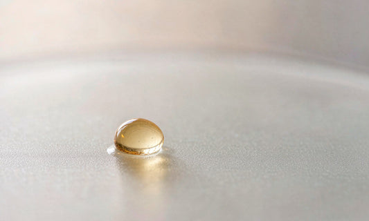 Macro close-up of a single translucent amber droplet resting on smooth frosted glass