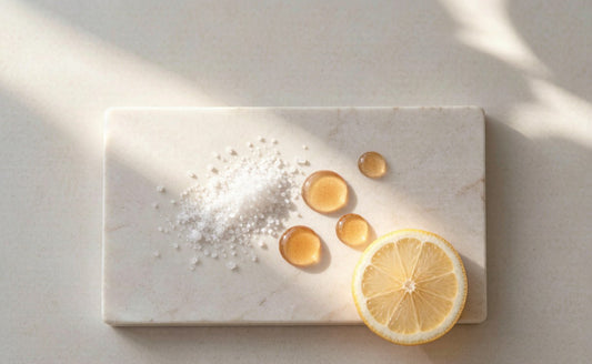 White mineral crystals and amber oil droplets beside a citrus slice on pale stone in warm sunlight