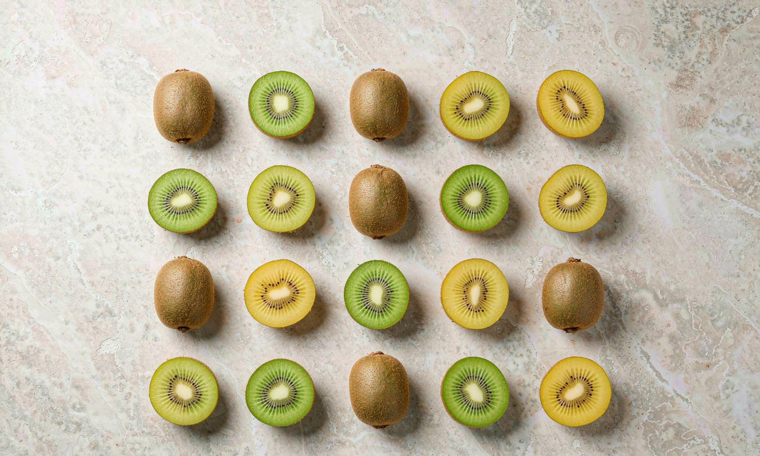 Overhead flat lay of whole and sliced green and golden kiwifruit arranged on a pale stone surface