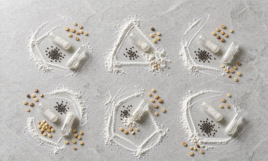 Abstract overhead arrangement of amino acid powder, capsules and seeds in a loose grid on pale stone