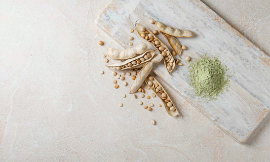Dried legume pods, seeds and a small mound of green powder on pale stone, natural ingredient still life