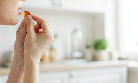 Hands holding a single amber gummy up to soft window light in a bright airy kitchen
