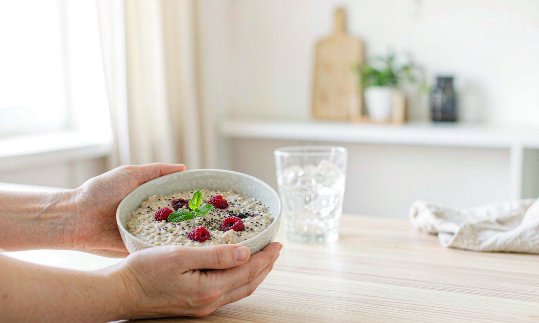 Pair of relaxed hands holding a ceramic bowl of oatmeal with berries on light wood counter
