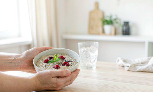 Pair of relaxed hands holding a ceramic bowl of oatmeal with berries on light wood counter